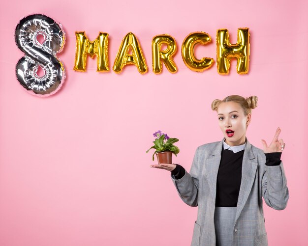 Vista frontal mujer joven sosteniendo pequeña flor con decoración de marzo sobre fondo rosa horizontal mujer color fiesta día de la mujer sensual igualdad presenta