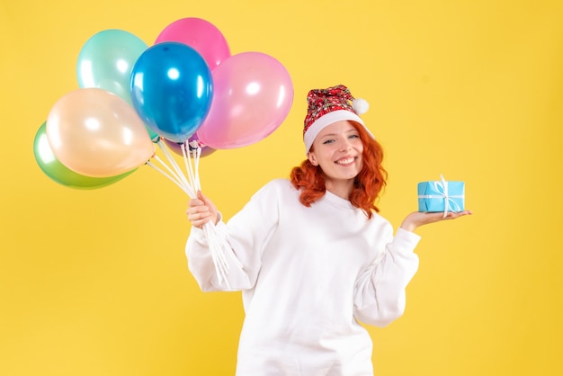 Foto gratuita vista frontal de la mujer joven sosteniendo pequeños globos de colores y presentes en la pared amarilla