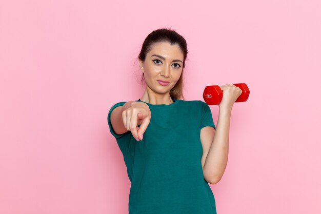 Vista frontal mujer joven sosteniendo pesas en la pared rosa atletas deporte ejercicio ejercicios de salud