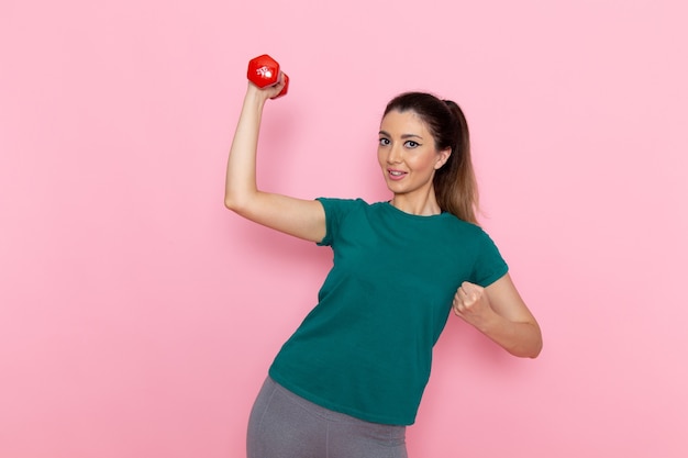 Vista frontal mujer joven sosteniendo pesas y sonriendo en la pared rosa atleta deporte ejercicio salud entrenamientos