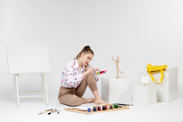 Vista frontal mujer joven sosteniendo pinturas para dibujar sobre fondo blanco.