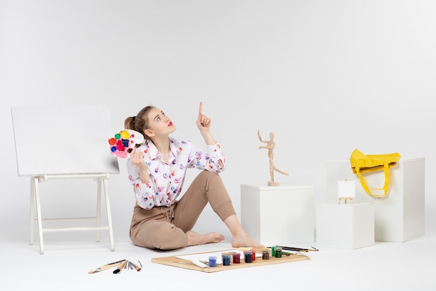 Vista frontal mujer joven sosteniendo pinturas para dibujar sobre fondo blanco.