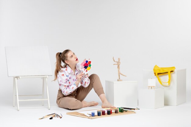 Vista frontal mujer joven sosteniendo pinturas para dibujar sobre fondo blanco.