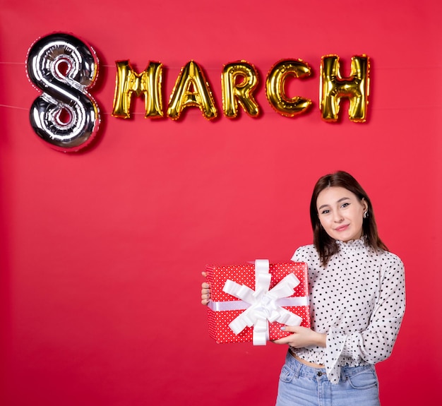 Foto gratuita vista frontal mujer joven sosteniendo presente de marzo sobre fondo rojo mujer cariñosa compras belleza horizontal vacaciones amor femenino igualdad