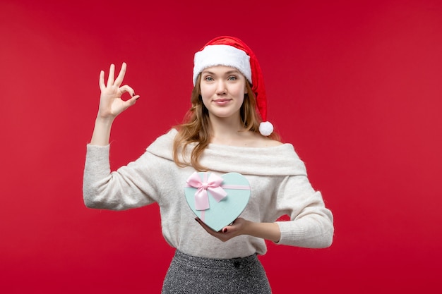 Vista frontal de la mujer joven sosteniendo presente en rojo piso rojo regalo navideño navideño