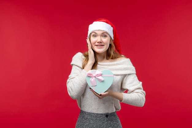 Vista frontal de la mujer joven sosteniendo presente en rojo piso rojo de regalo de vacaciones de Navidad