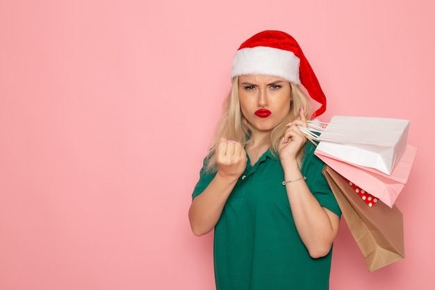 Vista frontal mujer joven sosteniendo regalos de navidad en paquetes en color de foto de año nuevo de vacaciones modelo de pared rosa