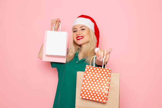 Vista frontal mujer joven sosteniendo regalos de navidad en paquetes en la pared rosa modelo de foto de navidad vacaciones de año nuevo