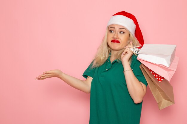 Vista frontal mujer joven sosteniendo regalos de navidad en paquetes en la pared rosa modelo vacaciones navidad año nuevo colores de la foto