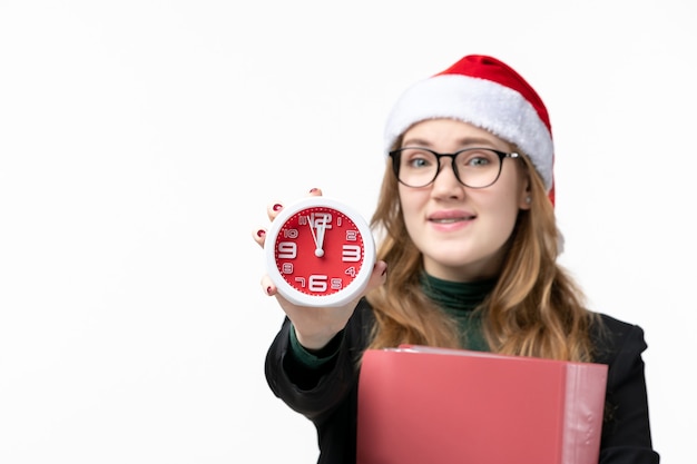 Vista frontal mujer joven sosteniendo el reloj con archivos en el libro de la universidad de lección de escritorio blanco