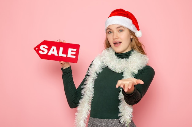 Foto gratuita vista frontal mujer joven sosteniendo rojo venta escribiendo en pared rosa vacaciones de navidad año nuevo compras moda emoción