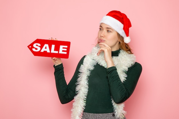 Vista frontal mujer joven sosteniendo rojo venta escribiendo en pared rosa vacaciones de navidad año nuevo foto compras moda emociones