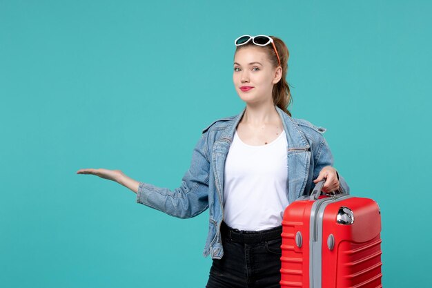 Vista frontal mujer joven sosteniendo su bolso rojo y preparándose para el viaje en el espacio azul