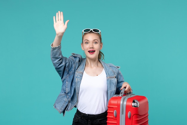 Vista frontal mujer joven sosteniendo su bolso rojo y preparándose para el viaje ondeando en el espacio azul