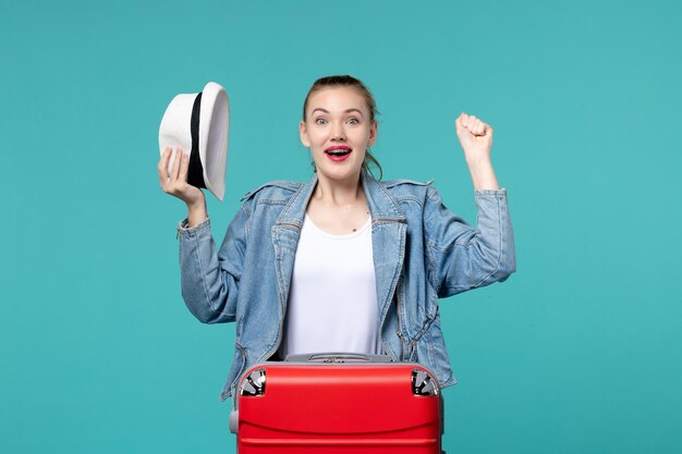 Vista frontal mujer joven sosteniendo su sombrero y preparándose para el viaje en el espacio azul claro