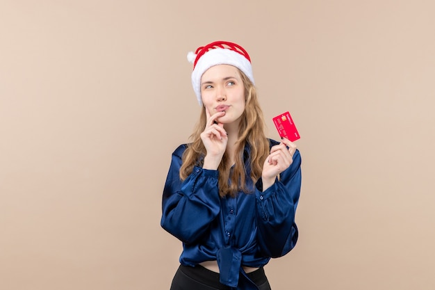 Vista frontal mujer joven sosteniendo una tarjeta bancaria roja sobre fondo rosa dinero vacaciones año nuevo navidad foto emoción lugar libre