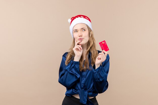 Vista frontal mujer joven sosteniendo una tarjeta bancaria roja sobre fondo rosa dinero vacaciones año nuevo navidad foto emoción lugar libre