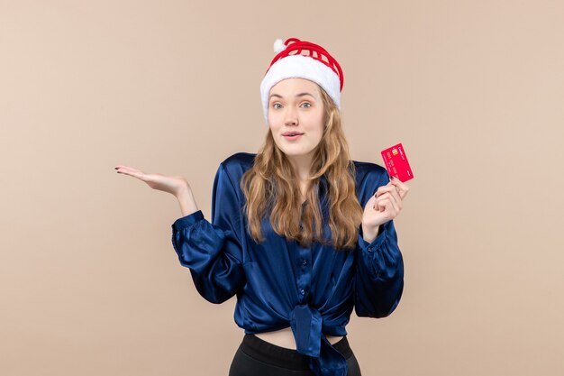 Vista frontal mujer joven sosteniendo una tarjeta bancaria roja sobre un fondo rosa foto de dinero de navidad vacaciones año nuevo emoción