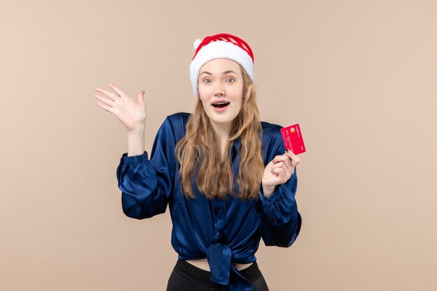 Vista frontal mujer joven sosteniendo una tarjeta bancaria roja sobre fondo rosa foto de dinero de navidad vacaciones año nuevo emoción