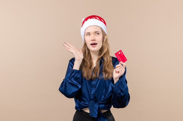 Vista frontal mujer joven sosteniendo una tarjeta bancaria roja sobre un fondo rosa foto de dinero vacaciones año nuevo emoción de navidad