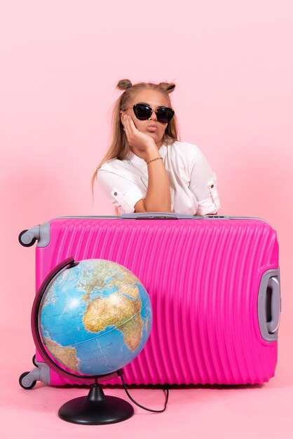 Vista frontal de la mujer joven con su bolso rosa preparándose para las vacaciones en la pared rosa