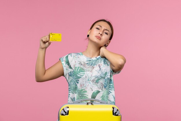 Vista frontal de la mujer joven con tarjeta bancaria amarilla y bolsa en una pared de color rosa claro