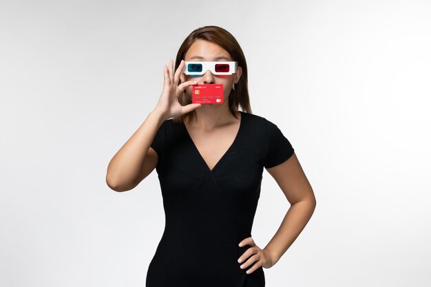 Vista frontal mujer joven con tarjeta bancaria en gafas de sol d sobre superficie blanca