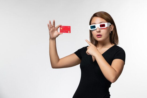 Vista frontal mujer joven con tarjeta bancaria en gafas de sol d sobre superficie blanca