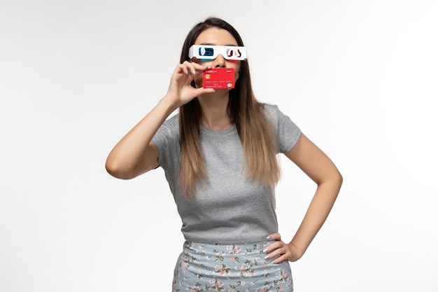 Vista frontal mujer joven con tarjeta bancaria en gafas de sol d sobre superficie blanca