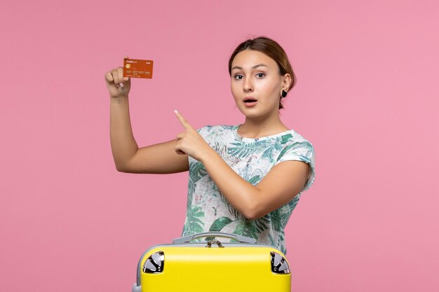 Vista frontal de la mujer joven con tarjeta bancaria marrón en la pared rosa