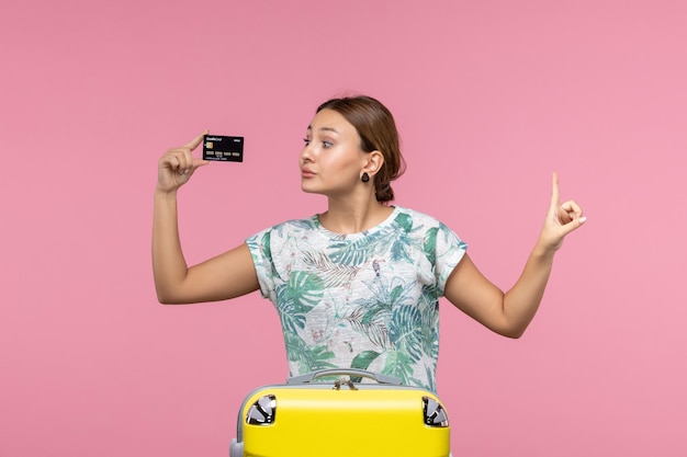 Vista frontal de la mujer joven con tarjeta bancaria negra en la pared rosa