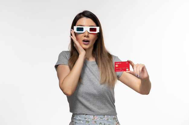 Vista frontal mujer joven con tarjeta bancaria roja en gafas de sol d en el escritorio blanco claro