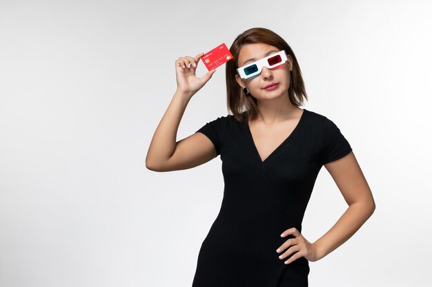 Vista frontal mujer joven con tarjeta bancaria roja en gafas de sol d sobre la superficie blanca clara