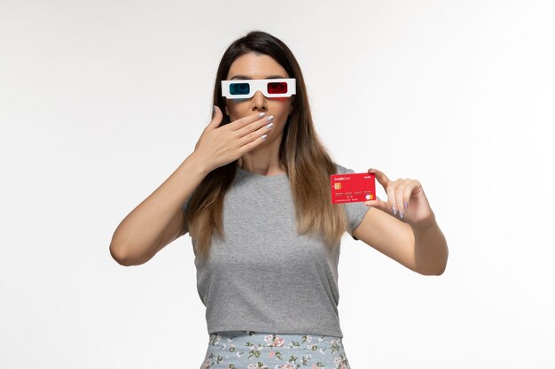 Vista frontal mujer joven con tarjeta bancaria roja en gafas de sol d sobre la superficie blanca clara