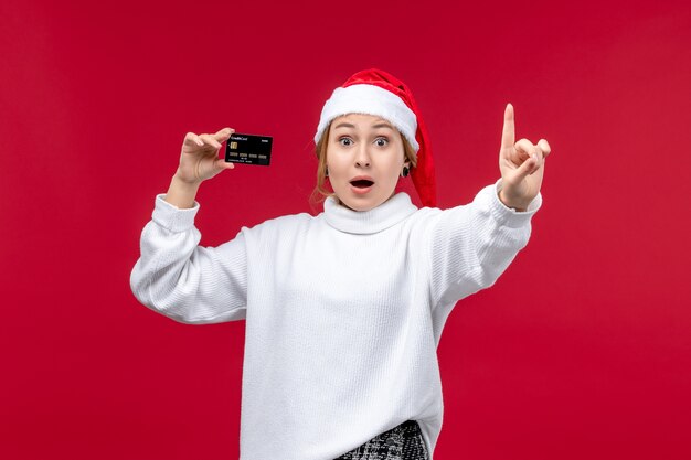 Vista frontal mujer joven con tarjeta bancaria sobre fondo rojo.