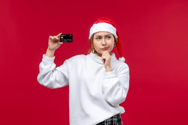 Vista frontal mujer joven con tarjeta bancaria sobre fondo rojo.