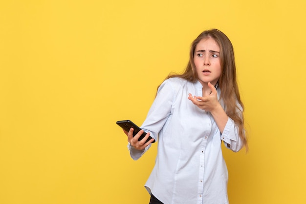 Vista frontal, de, mujer joven, con, teléfono, en, pared amarilla