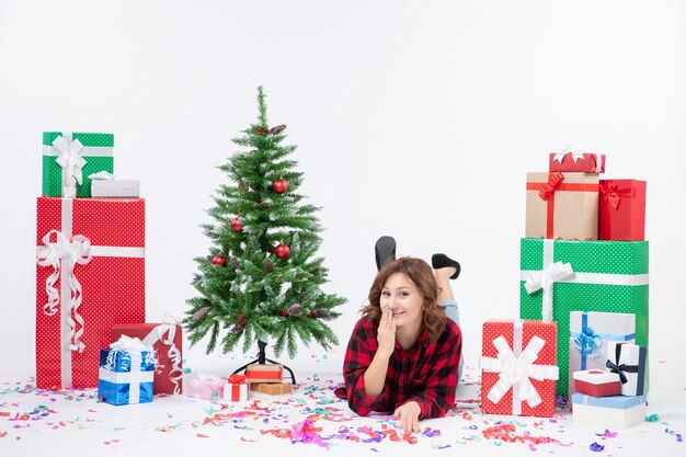 Vista frontal mujer joven tendido alrededor de regalos de Navidad y árbol de vacaciones sobre fondo blanco regalo de año nuevo de Navidad color nieve emociones