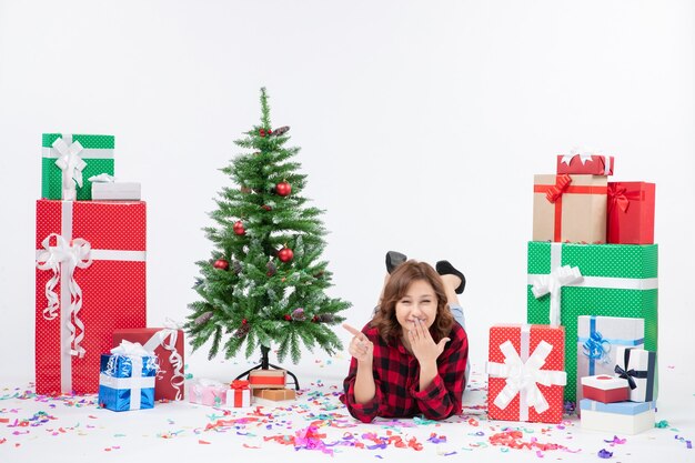 Vista frontal mujer joven tendido alrededor de regalos de navidad y árbol de vacaciones sobre fondo blanco regalo navidad año nuevo color nieve