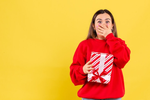 Foto gratuita vista frontal, de, mujer joven, tenencia, pequeño, regalo, conmocionado, en, pared amarilla