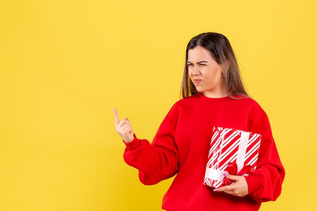 Vista frontal, de, mujer joven, tenencia, pequeño, regalo, en, un, pared amarilla