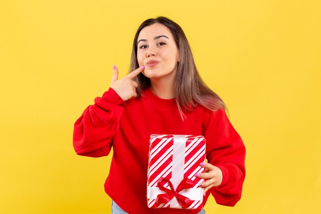 Vista frontal, de, mujer joven, tenencia, pequeño, regalo, en, un, pared amarilla