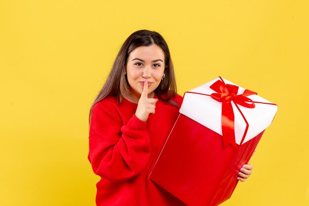 Vista frontal, de, mujer joven, tenencia, regalo de navidad, en, pared amarilla