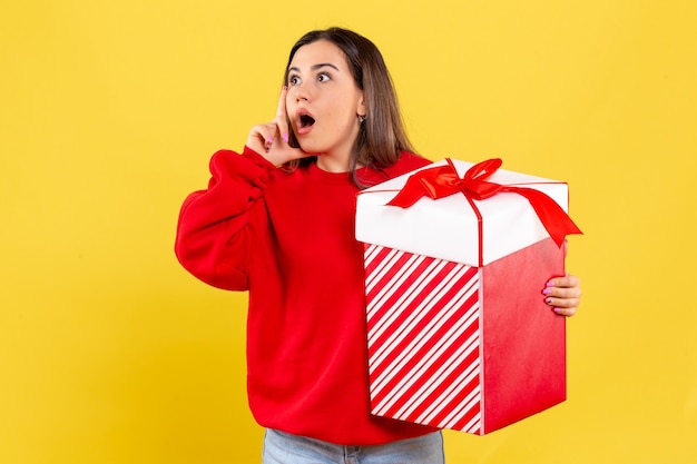 Foto gratuita vista frontal, de, mujer joven, tenencia, regalo de navidad, en, pared amarilla