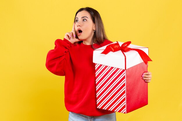 Vista frontal, de, mujer joven, tenencia, regalo de navidad, en, pared amarilla