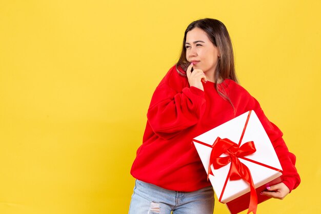 Vista frontal, de, mujer joven, tenencia, regalo de navidad, en, pared amarilla