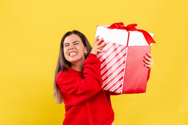 Vista frontal, de, mujer joven, tenencia, regalo de navidad, en, pared amarilla