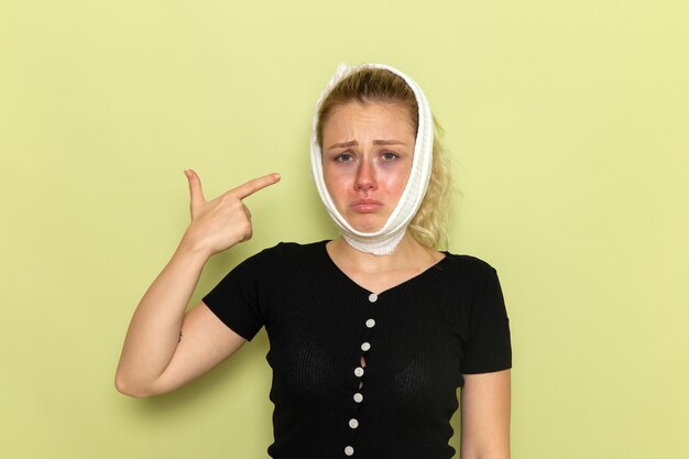 Vista frontal de una mujer joven con una toalla blanca alrededor de la cabeza sintiéndose muy enferma y enferma de dolor de muelas en el escritorio verde enfermedad enfermedad salud femenina niña