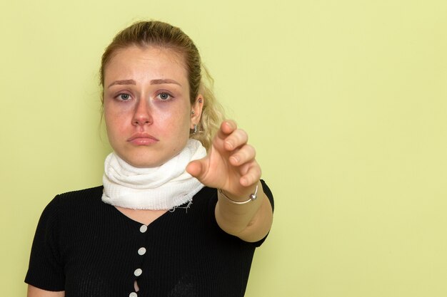 Vista frontal mujer joven con una toalla blanca alrededor de su garganta sintiéndose muy enferma y enferma en la pared verde claro enfermedad enfermedad salud femenina