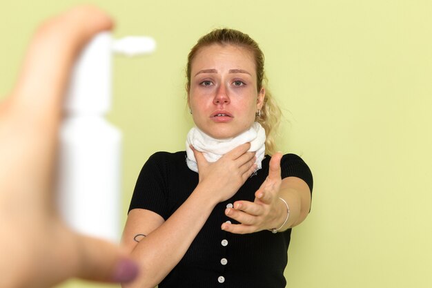 Vista frontal mujer joven con una toalla blanca alrededor de su garganta sintiéndose muy enferma y enferma en la pared verde enfermedad enfermedad salud femenina